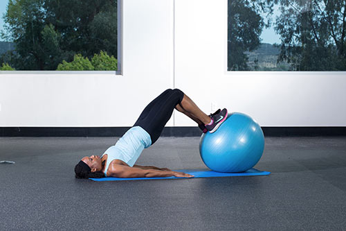 Using a mat and exercise ball to perform a bridging exercise.
