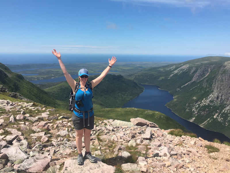 Female hiker at Gros Morne Mountain Summit with Ten Mile Pond in background.