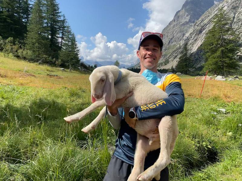 Male trail runner holding a lamb on the Tour du Mont Blanc trail.