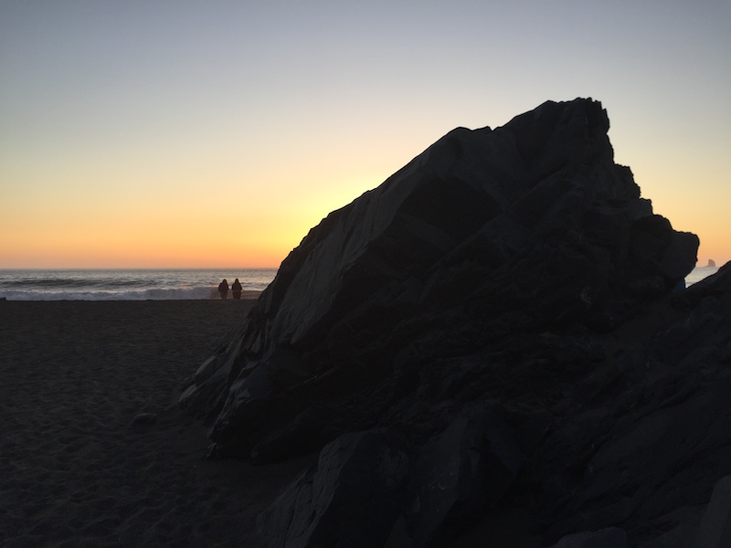 Two people standing on Oregon Coast beach watching sunset.