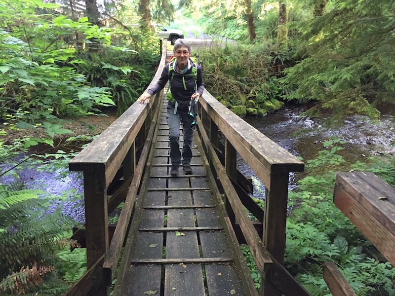 Hiker walking over suspension bridge over Arch Cape Creek on Oregon Coast Trail.